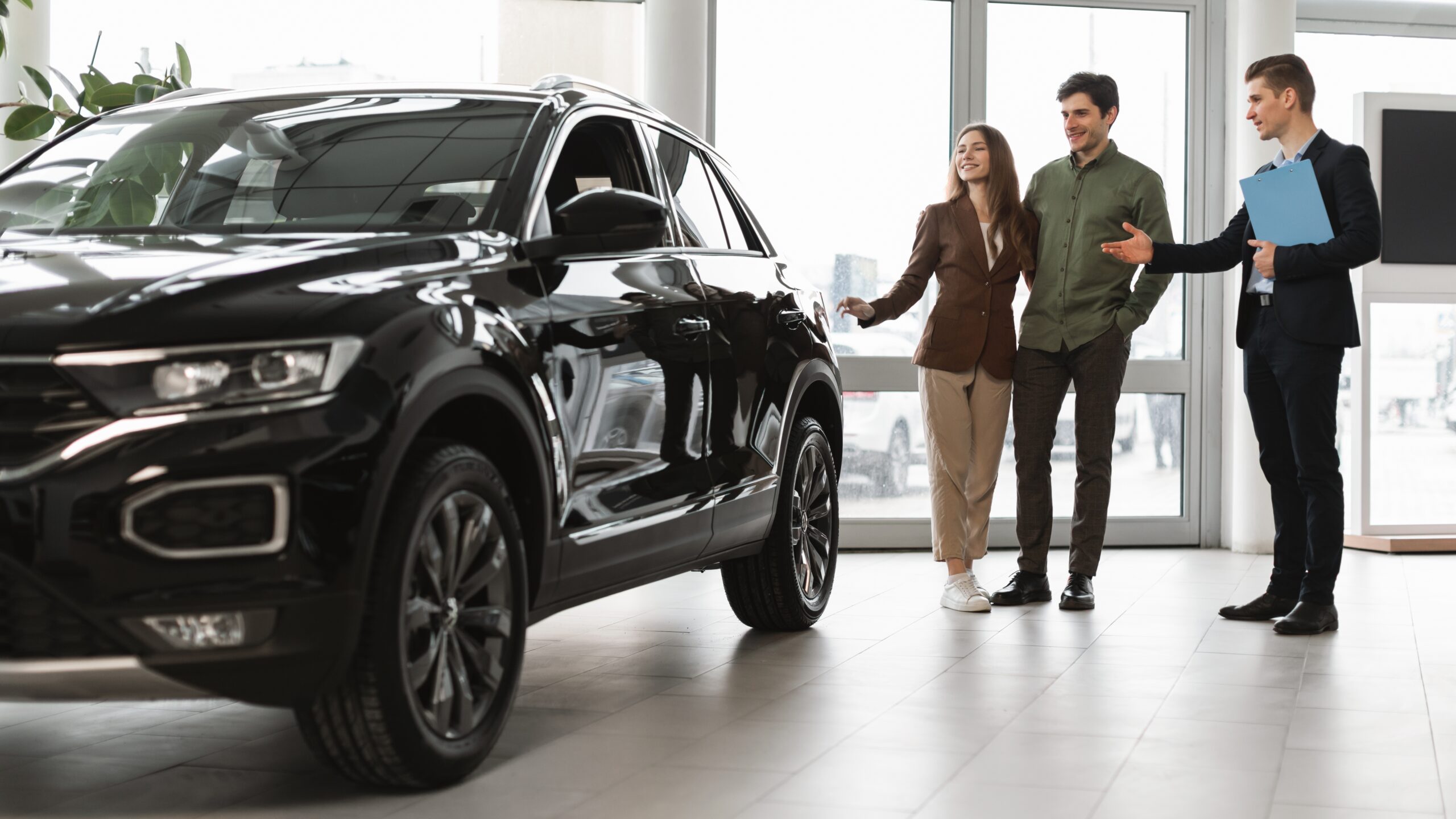 Confident,Car,Salesman,Showing,New,Car,To,Millennial,Couple,At